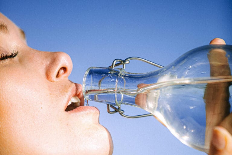 Frau trinkt aus einer Glasflasche, blauer Himmel Frau trinkt aus einer Glasflasche, blauer Himmel